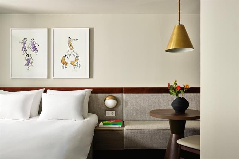 The rooms feature a double bed, integrated seating and wall-mounted lighting. The interior combines textiles, wood finishes and framed artwork.